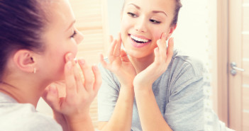 Beauty skin care. Young beautiful teenage girl touching her face before the mirror, enjoying her clean skin. Pretty woman touching her cheek and smiling. Perfect pure skin. Fresh Clean Skin. Skincare